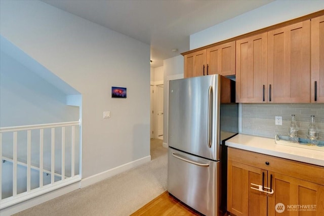 kitchen featuring baseboards, light countertops, decorative backsplash, freestanding refrigerator, and brown cabinetry