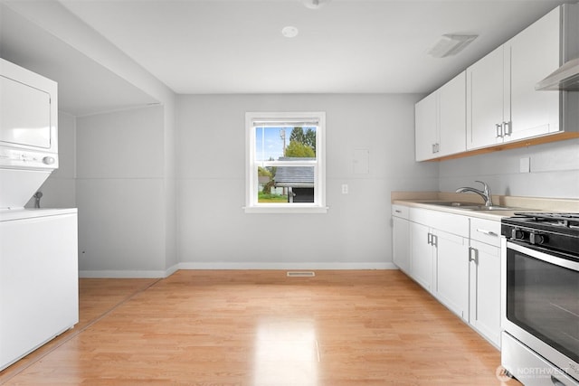 interior space featuring gas stove, light wood-style flooring, a sink, white cabinetry, and stacked washer / dryer