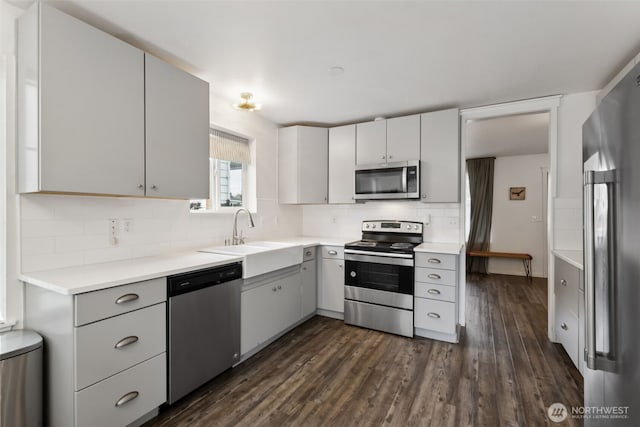 kitchen featuring dark wood-type flooring, a sink, backsplash, stainless steel appliances, and light countertops