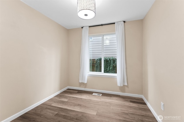 empty room featuring visible vents, wood finished floors, and baseboards