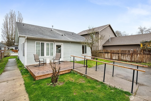 back of property featuring a deck, fence, a lawn, and a shingled roof