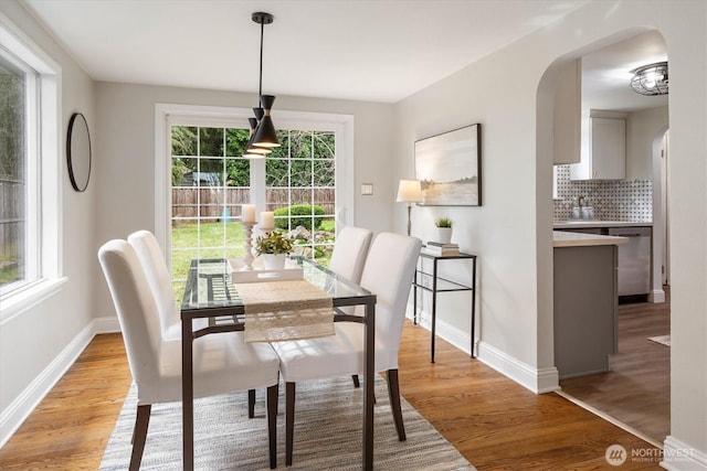 dining room with arched walkways, baseboards, and light wood finished floors