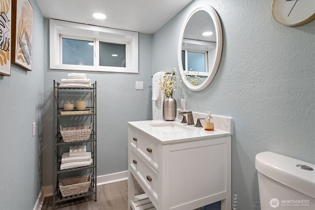 half bath featuring baseboards, toilet, wood finished floors, a textured wall, and vanity