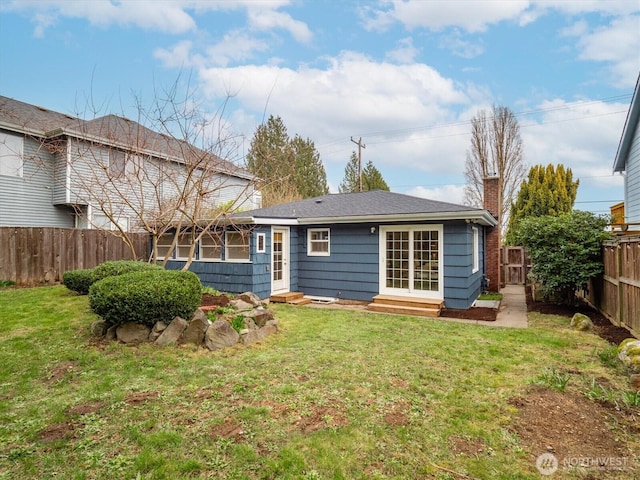 rear view of house with entry steps, a yard, a fenced backyard, and a chimney