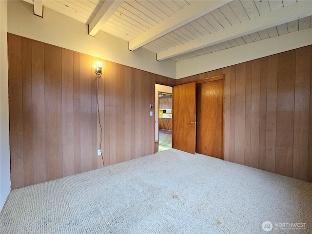 carpeted empty room with beam ceiling, wood walls, and wooden ceiling