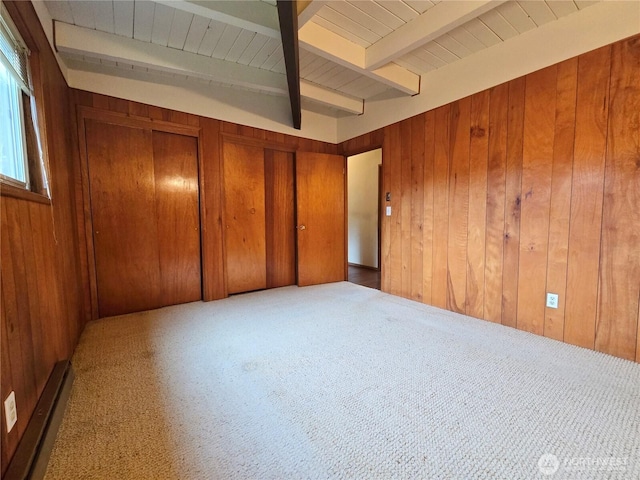 unfurnished bedroom featuring wooden walls, beamed ceiling, two closets, and carpet flooring