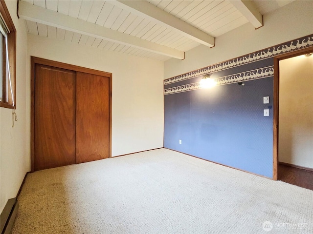 unfurnished bedroom with a closet, beam ceiling, carpet floors, and wooden ceiling