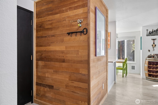 hall with wooden walls, visible vents, and light wood finished floors