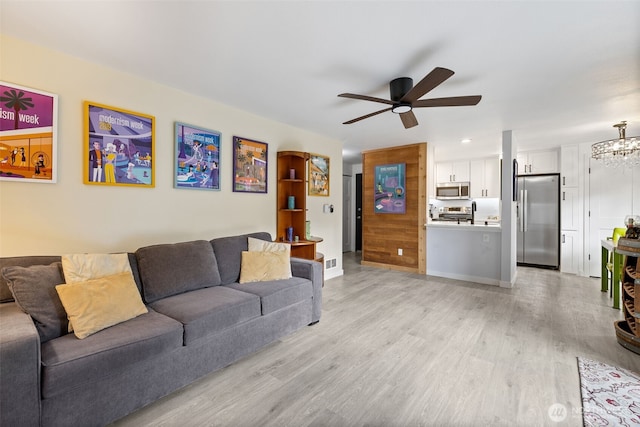 living room featuring light wood-type flooring, baseboards, visible vents, and ceiling fan with notable chandelier