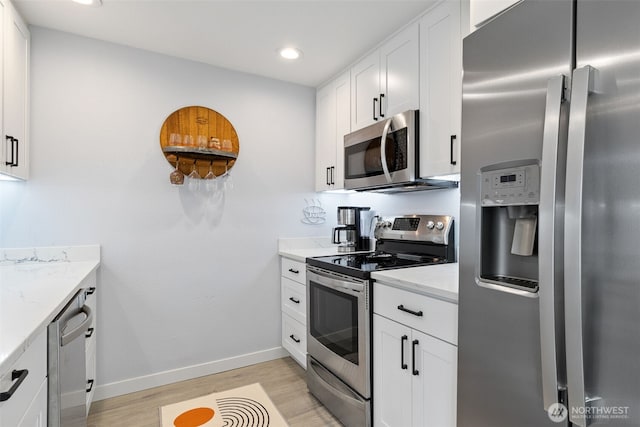 kitchen with light wood finished floors, appliances with stainless steel finishes, white cabinetry, and light stone countertops