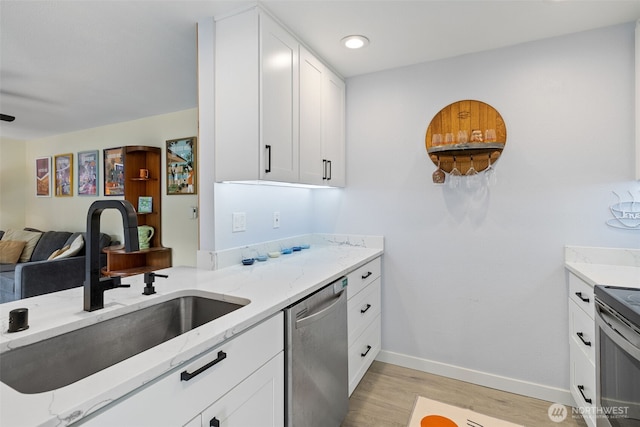 kitchen featuring light wood finished floors, light stone countertops, open floor plan, stainless steel appliances, and a sink