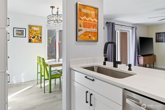 kitchen with light stone counters, white cabinetry, a sink, light wood-style floors, and stainless steel dishwasher