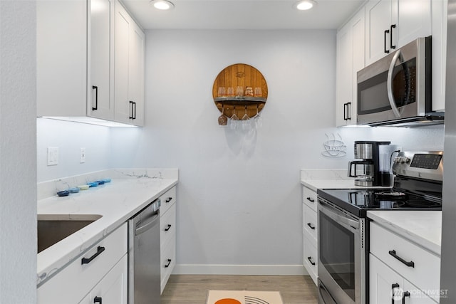 kitchen with light stone counters, light wood finished floors, appliances with stainless steel finishes, and white cabinetry