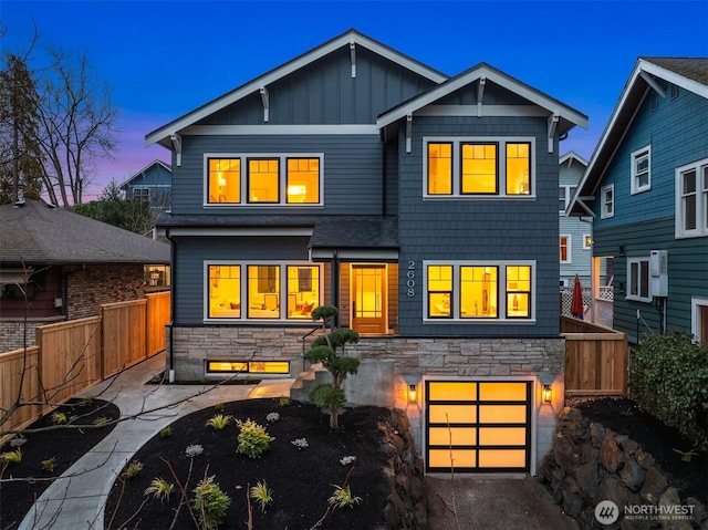 back of property at dusk featuring a garage, stone siding, board and batten siding, and fence