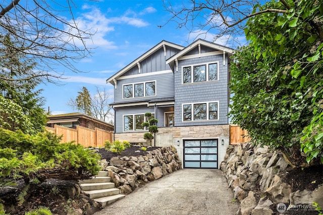 view of front of house with fence, driveway, a garage, stone siding, and board and batten siding