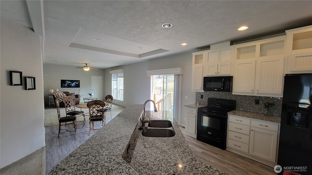kitchen featuring light stone countertops, a tray ceiling, a sink, decorative backsplash, and black appliances
