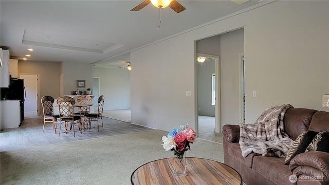 carpeted living area featuring ornamental molding, a ceiling fan, a tray ceiling, wood finished floors, and recessed lighting