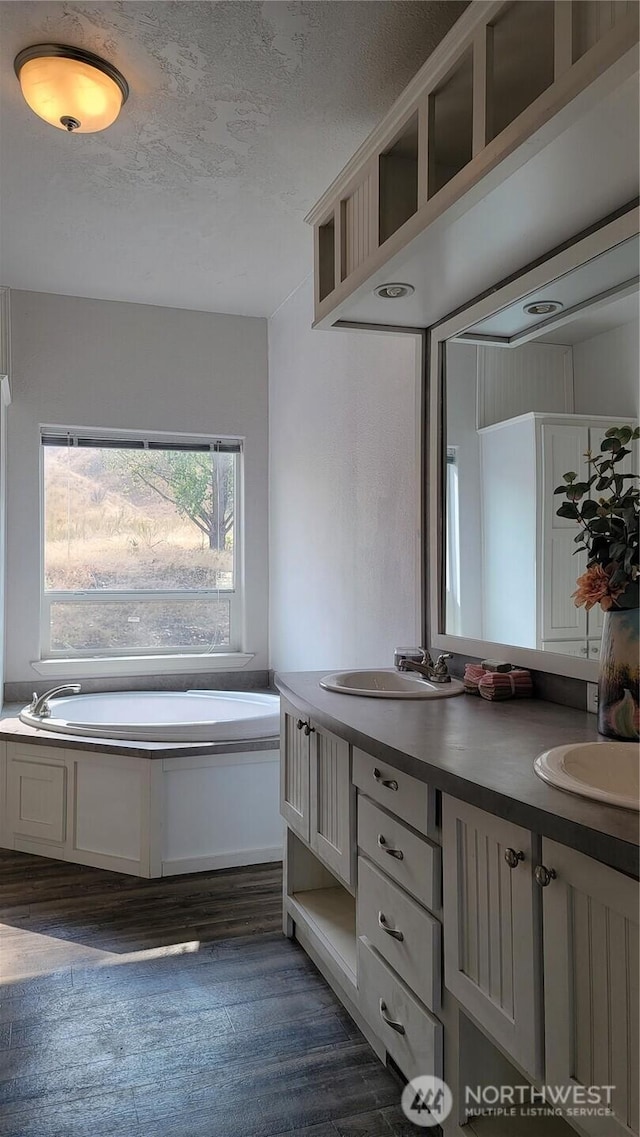 full bathroom with a textured ceiling, a bath, wood finished floors, and a sink