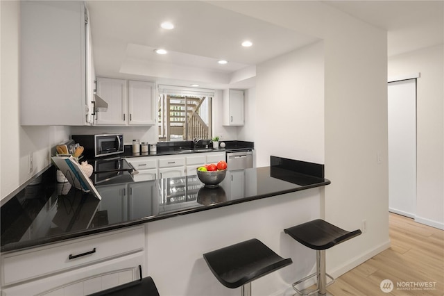 kitchen featuring dark countertops, a tray ceiling, recessed lighting, appliances with stainless steel finishes, and a peninsula