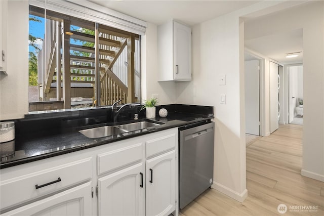 kitchen with light wood-style flooring, a sink, dark countertops, white cabinetry, and dishwasher