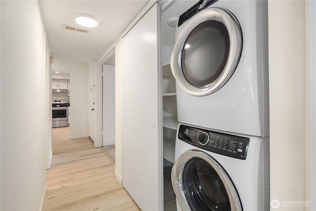 laundry area featuring light wood finished floors, visible vents, stacked washing maching and dryer, and laundry area