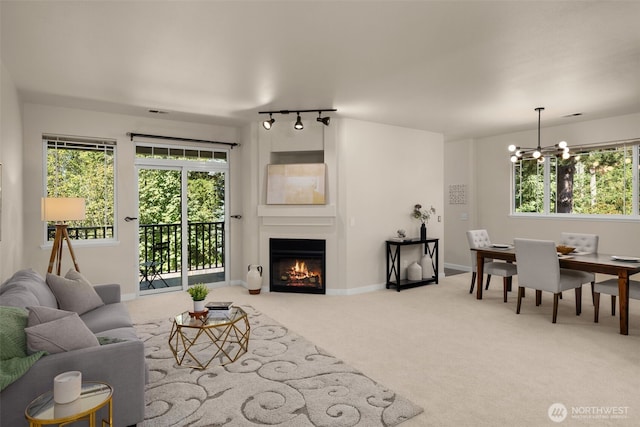 carpeted living room featuring a notable chandelier, baseboards, and a warm lit fireplace