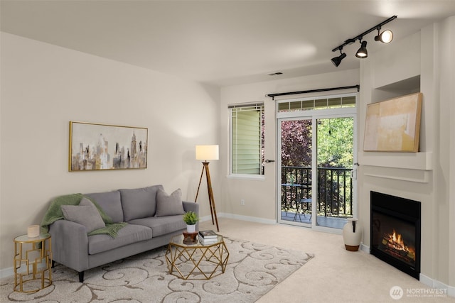 living room with a glass covered fireplace, baseboards, track lighting, and carpet