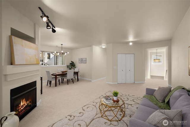 living area with baseboards, carpet floors, an inviting chandelier, track lighting, and a glass covered fireplace