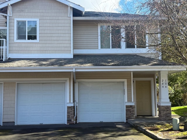 view of front of home with stone siding, an attached garage, driveway, and roof with shingles