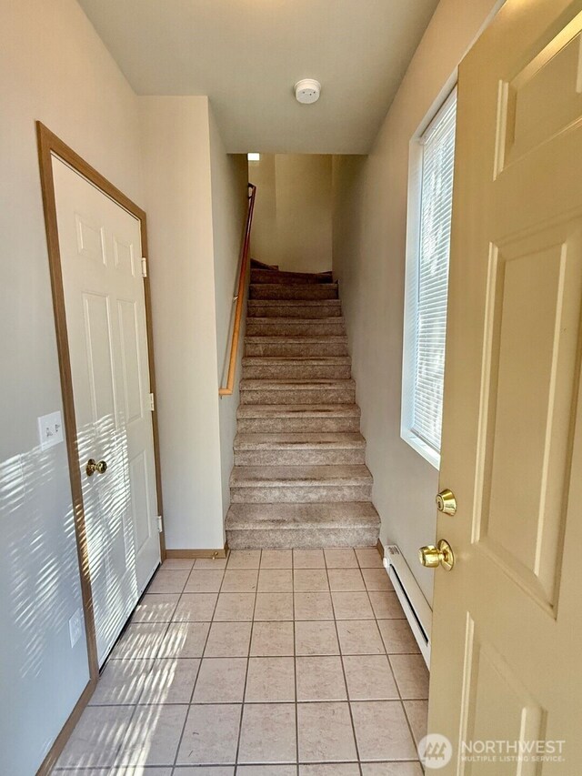 stairs with a wealth of natural light, a baseboard radiator, and tile patterned flooring