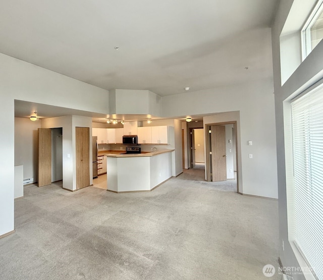 kitchen featuring a peninsula, appliances with stainless steel finishes, light carpet, white cabinetry, and open floor plan