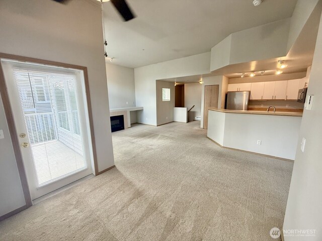 unfurnished living room featuring a glass covered fireplace, light colored carpet, and baseboards