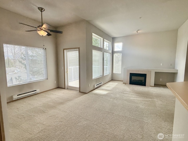 unfurnished living room featuring a tiled fireplace, a healthy amount of sunlight, baseboard heating, and carpet floors