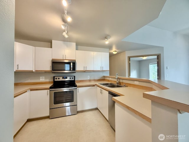 kitchen featuring light countertops, a peninsula, white cabinets, stainless steel appliances, and a sink