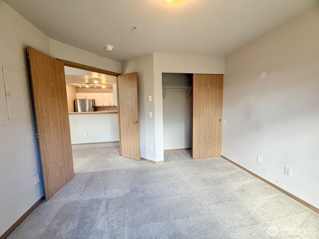 unfurnished bedroom with a closet, freestanding refrigerator, baseboards, and carpet floors