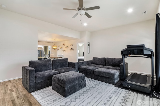 living room featuring light wood-type flooring, baseboards, and ceiling fan with notable chandelier