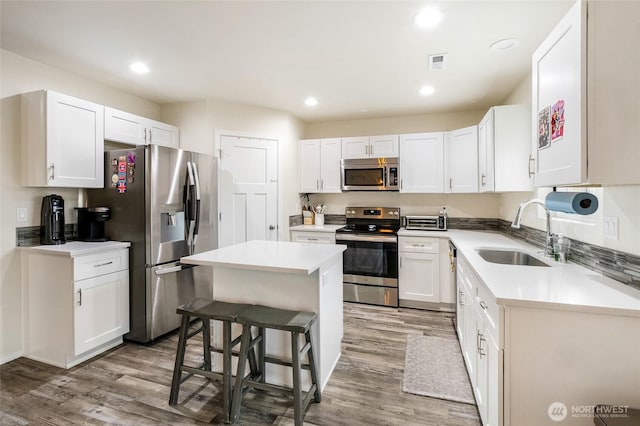 kitchen featuring appliances with stainless steel finishes, white cabinetry, light wood-style floors, and a sink