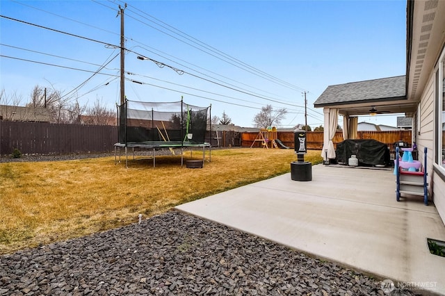 view of yard featuring a patio, a trampoline, a fenced backyard, and a playground