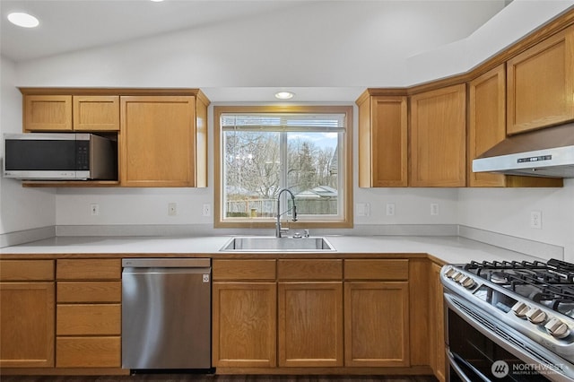 kitchen with under cabinet range hood, light countertops, vaulted ceiling, appliances with stainless steel finishes, and a sink