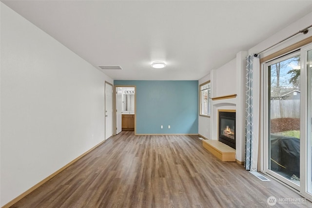 unfurnished living room featuring a glass covered fireplace, plenty of natural light, wood finished floors, and visible vents