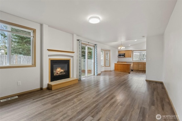 unfurnished living room with visible vents, baseboards, vaulted ceiling, wood finished floors, and a glass covered fireplace