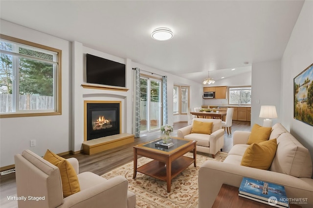 living area featuring lofted ceiling, a healthy amount of sunlight, a glass covered fireplace, and light wood finished floors