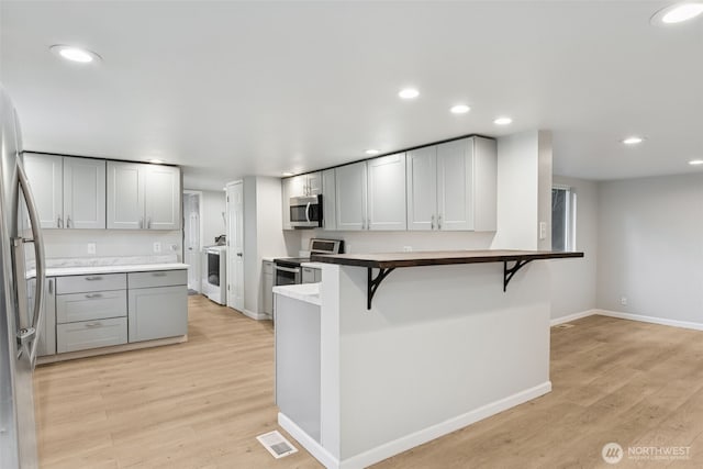 kitchen with recessed lighting, appliances with stainless steel finishes, a kitchen bar, and light wood-style floors