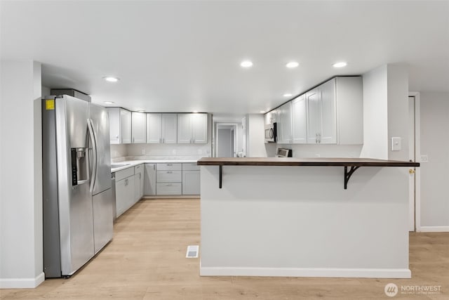 kitchen featuring a kitchen breakfast bar, light wood-style floors, appliances with stainless steel finishes, and a peninsula