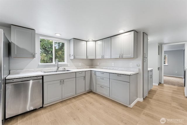 kitchen featuring a sink, gray cabinetry, light countertops, dishwasher, and light wood-type flooring