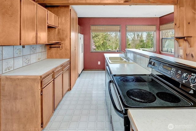 kitchen featuring a sink, backsplash, range with electric stovetop, light countertops, and light floors