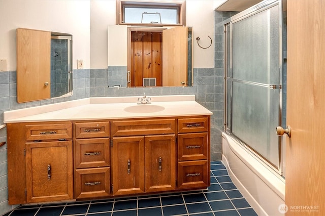 bathroom featuring vanity, visible vents, shower / bath combination with glass door, tile walls, and tile patterned floors