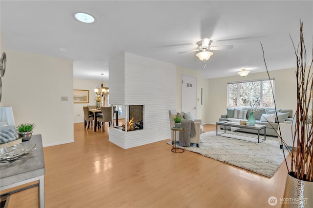 living room featuring baseboards, a multi sided fireplace, wood finished floors, and ceiling fan with notable chandelier