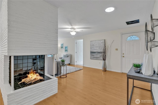 entrance foyer featuring a ceiling fan, visible vents, wood finished floors, baseboards, and a multi sided fireplace