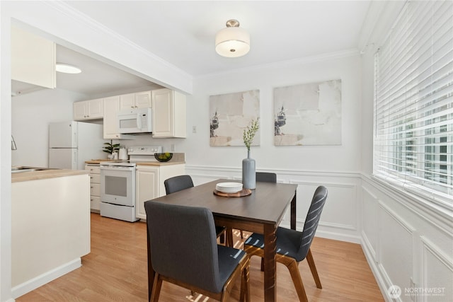 dining area featuring light wood-style flooring, ornamental molding, wainscoting, and a decorative wall